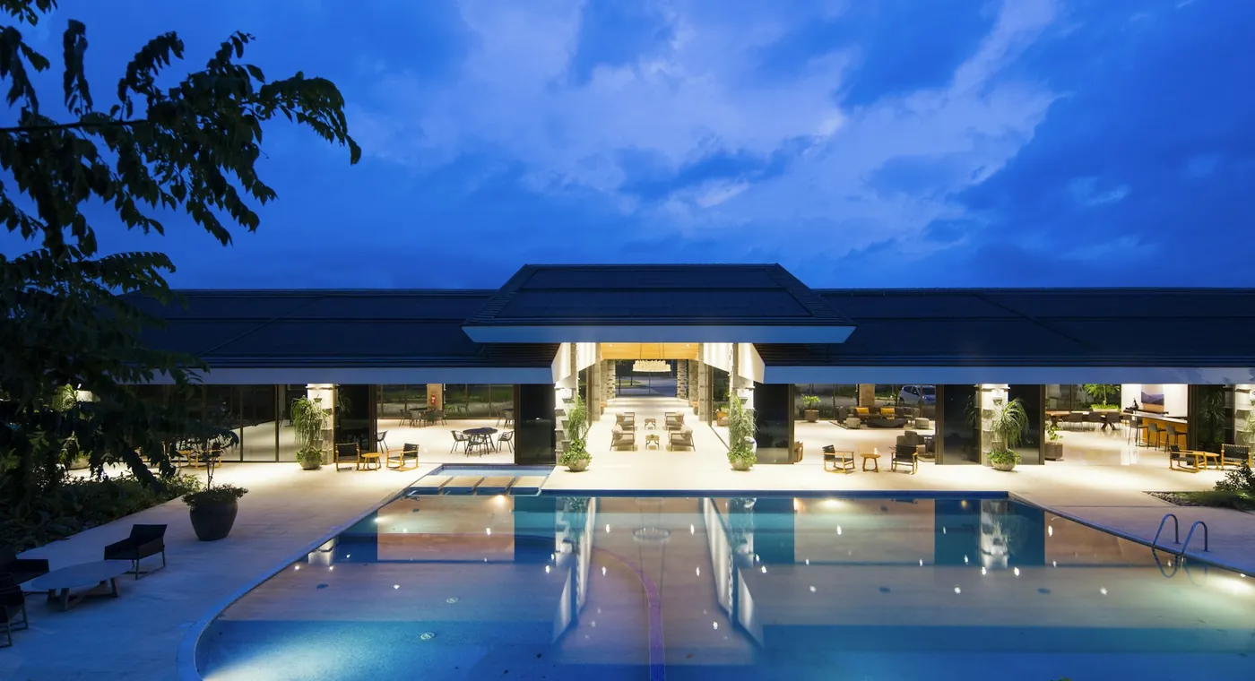 A quiet luxury resort pavilion at dusk, warm gold light reflecting on a still pool